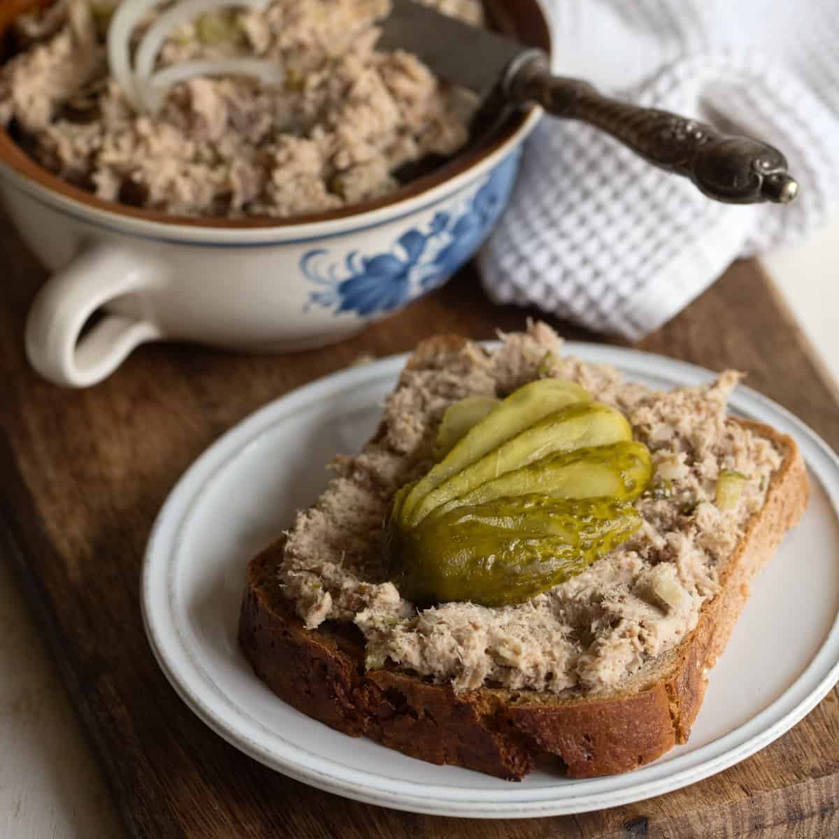 Leftover pork roast spread on a slice of rye bread, served on a small plate. Garnished with a gherkin.