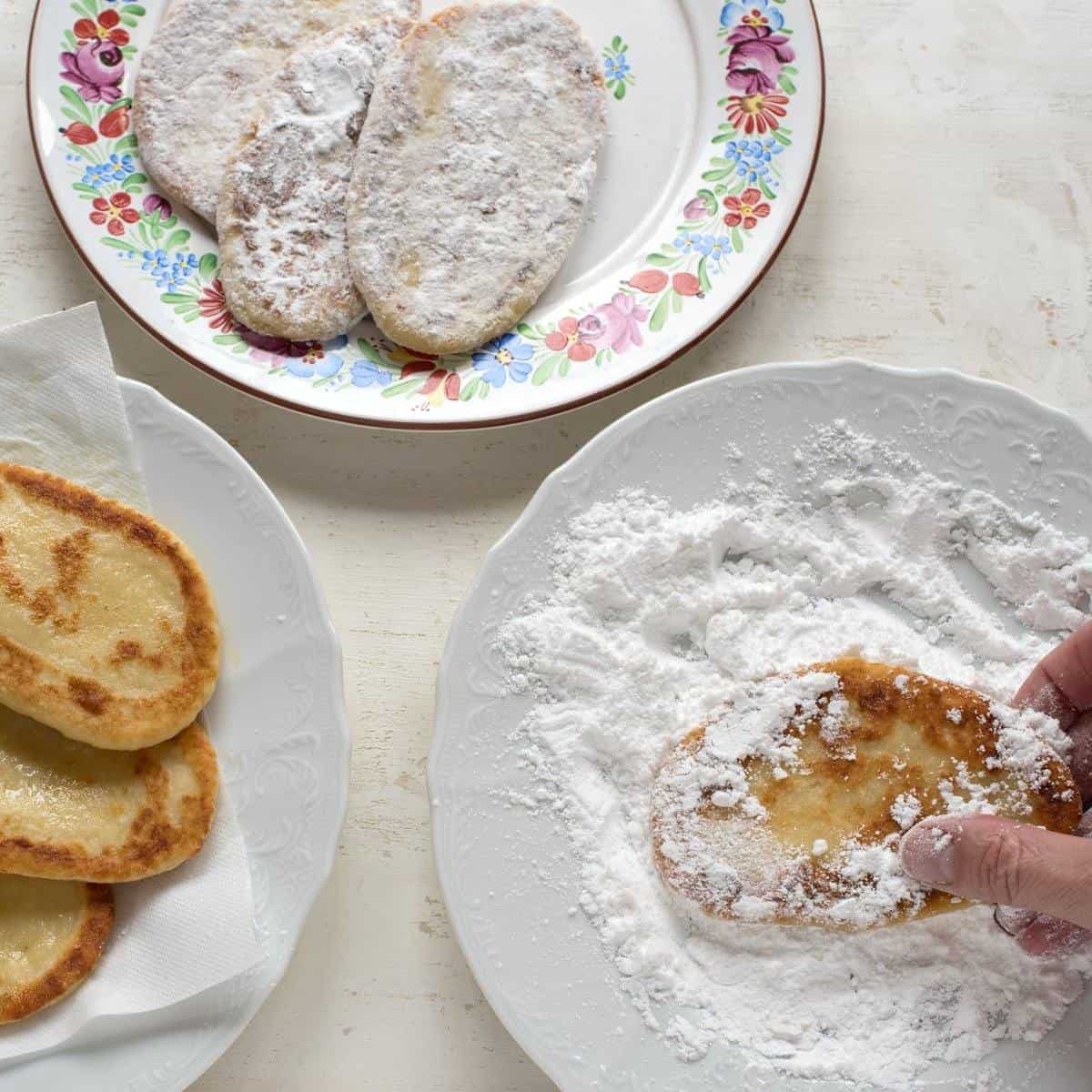 Coating fried farmers cheese pancakes in powdered sugar.