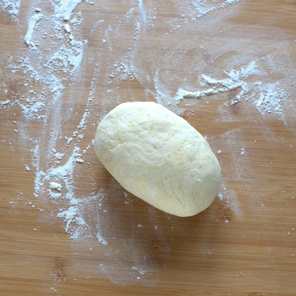 Farmers cheese dough shaped into a cylinder, placed on a floured surface.