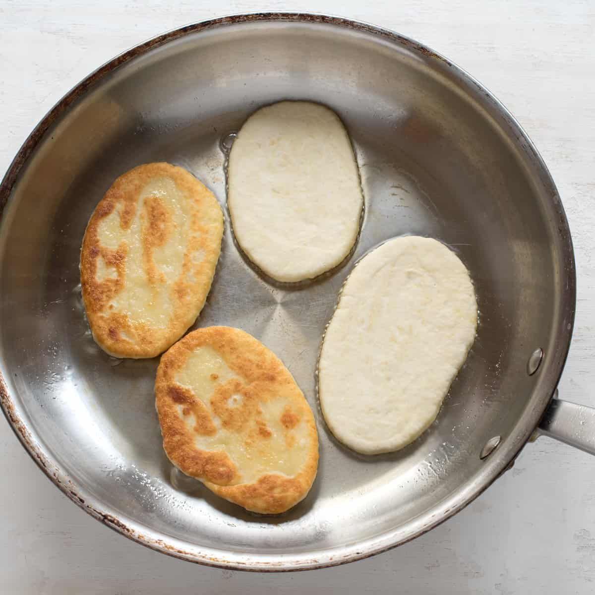Four pancakes are fryining in a stainless steel pan.