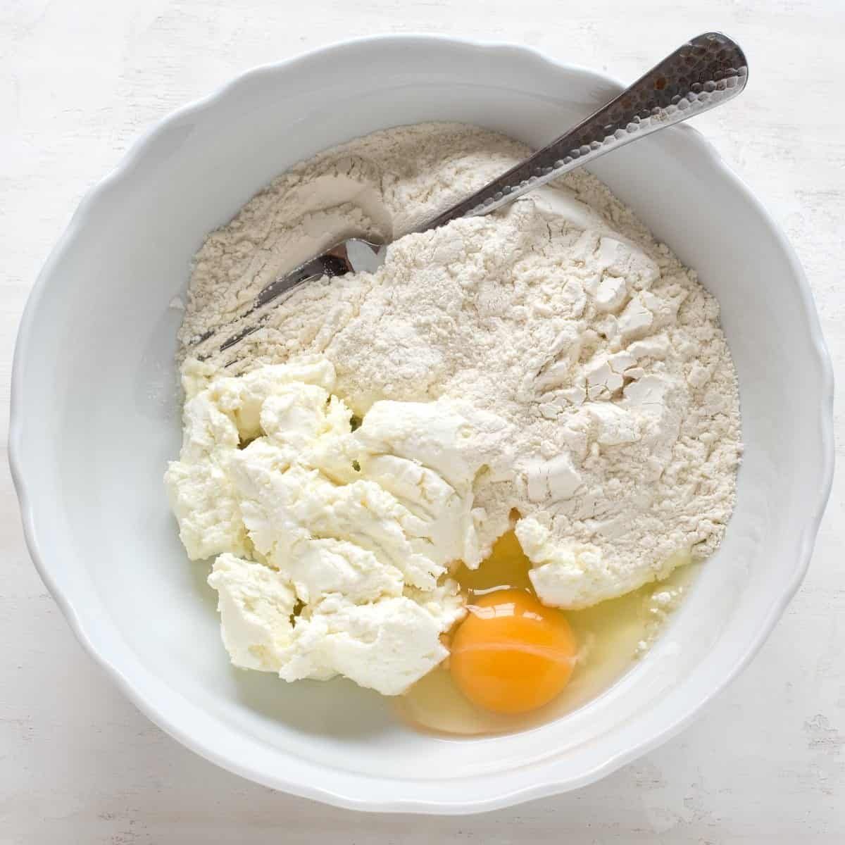 Ingredients for farmers cheese dough in a white bowl, a fork included.