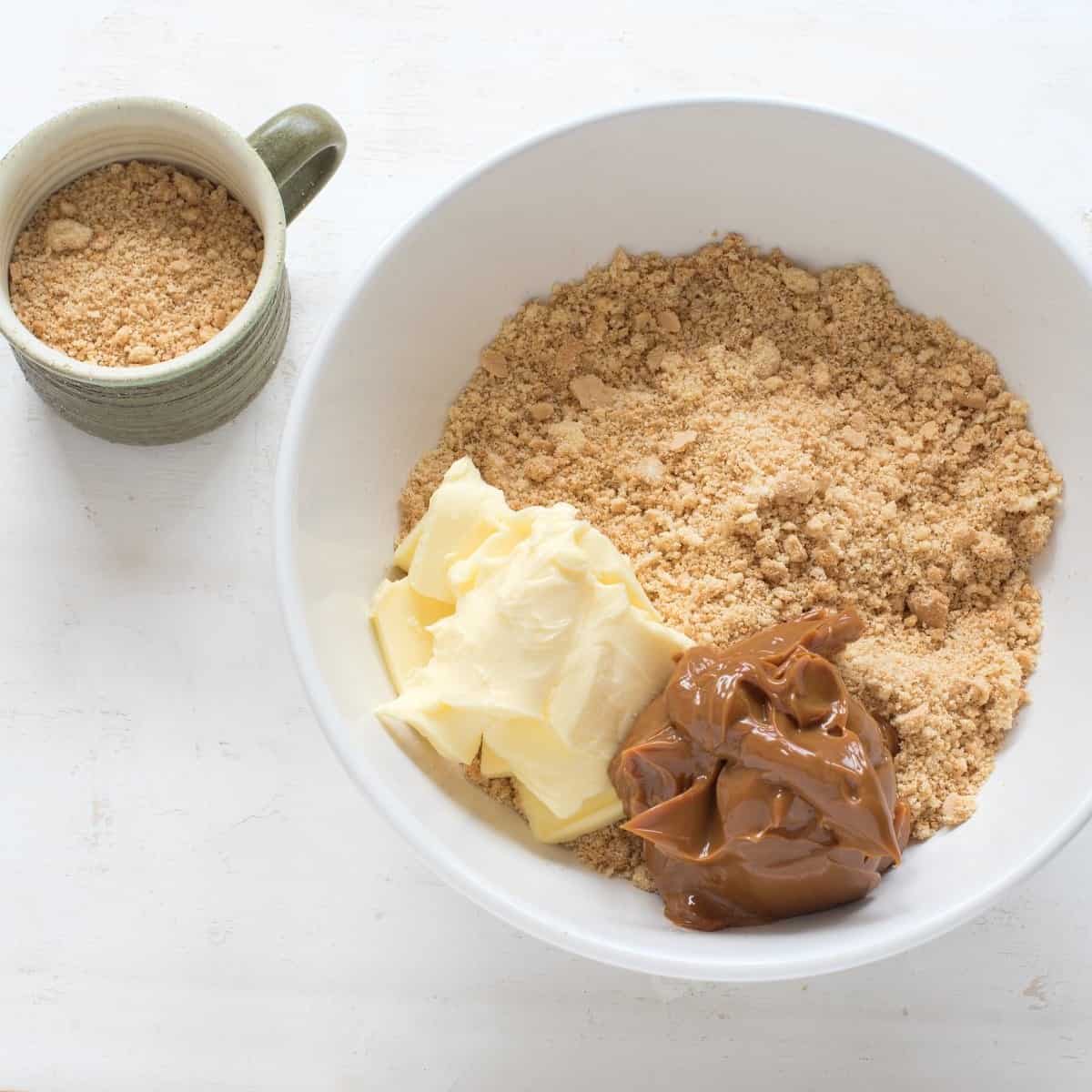 Preparing a soft dough mixture of crumbs, softened butter, and caramelized sweetened condensed milk, with a cup of crumbs placed on the left.