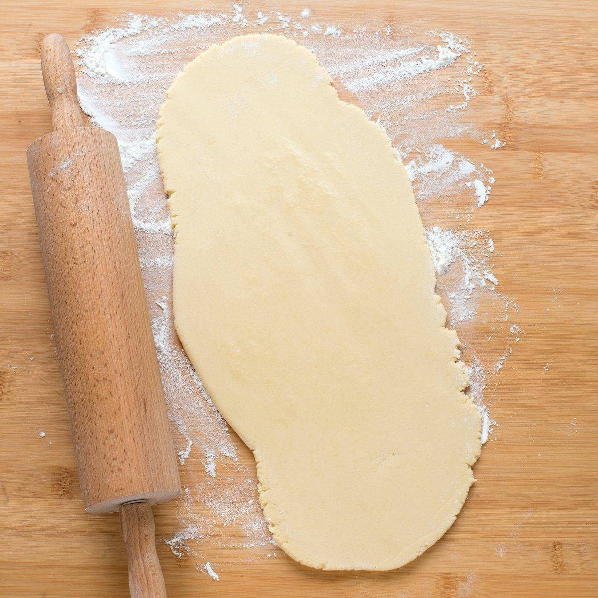 On the floured work surface, honey dough is being rolled out with a rolling pin positioned on the left side.