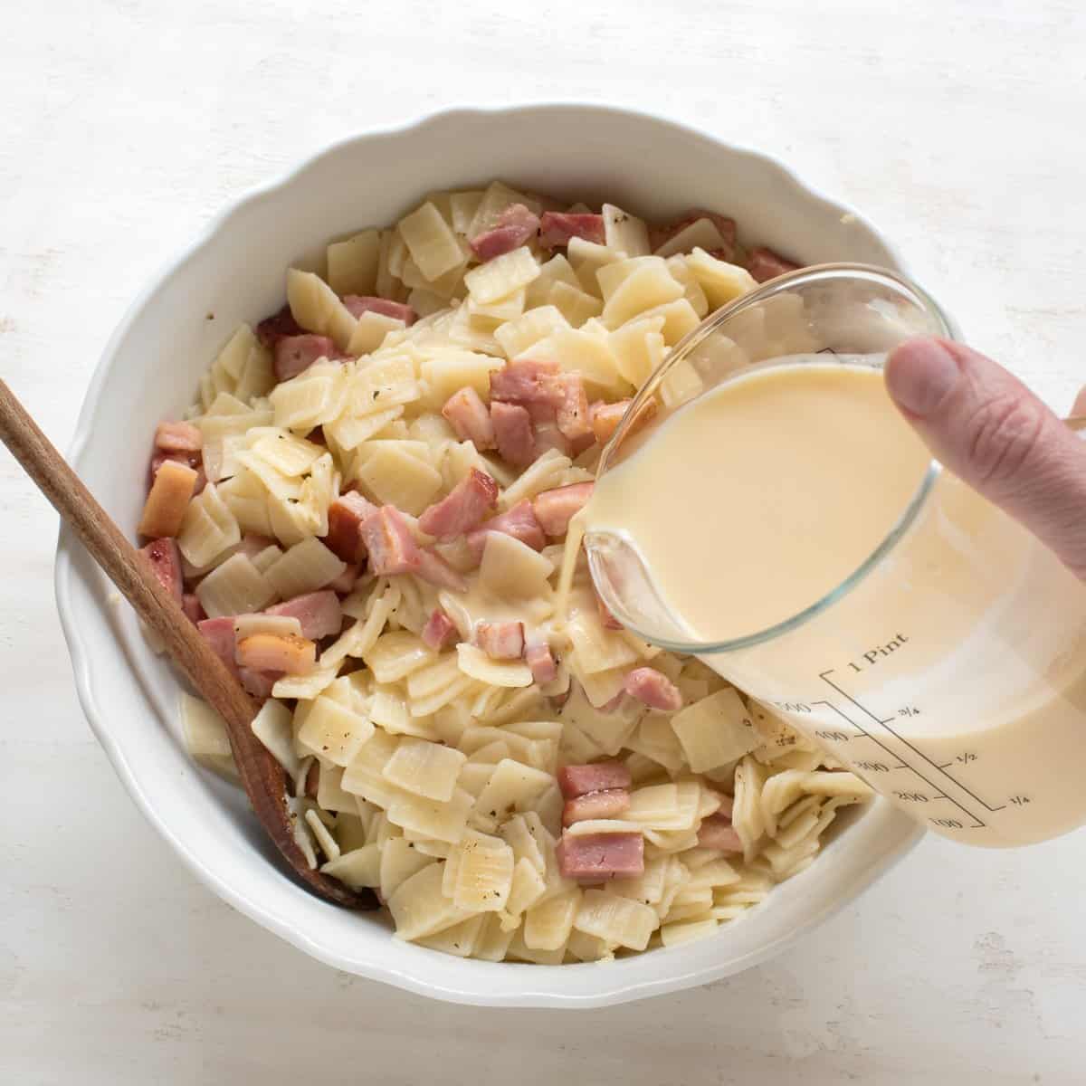 Pouring an eggy mixture over noodle and ham.