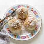 Three cherry dumplings topped with cinnamon sugar, served on a plate.