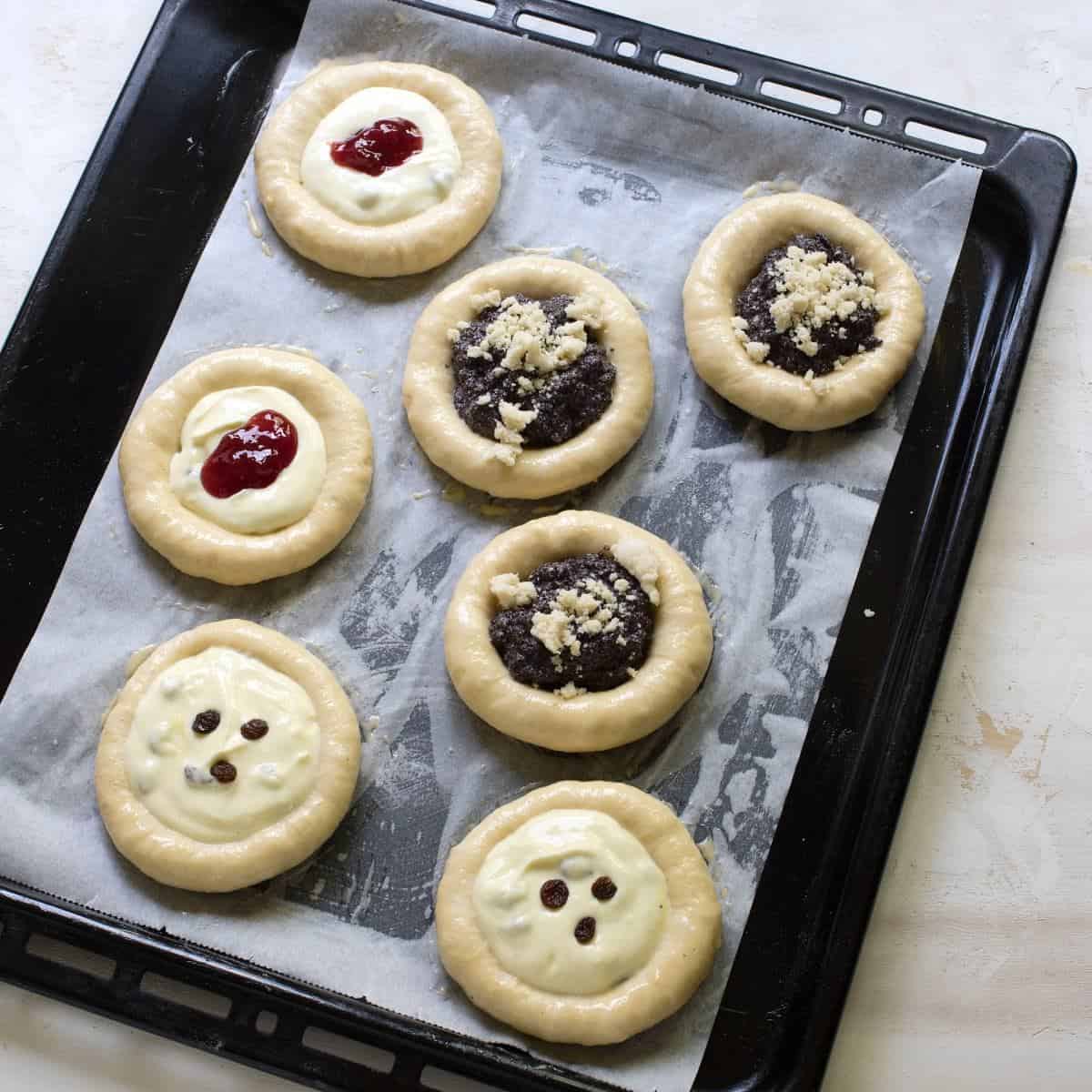 Seven pieces of Czech kolache on a baking sheet, before baking.