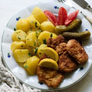 Czech řízek served with potatoes, dill pickles and wedges of tomatoes.
