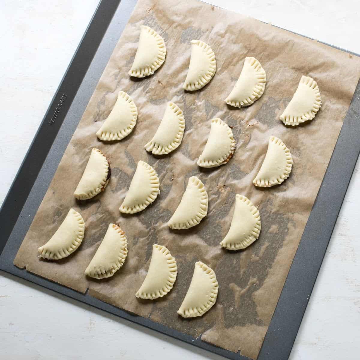Filled farmers cheese dough crescents on a baking sheet lined with parchment paper.