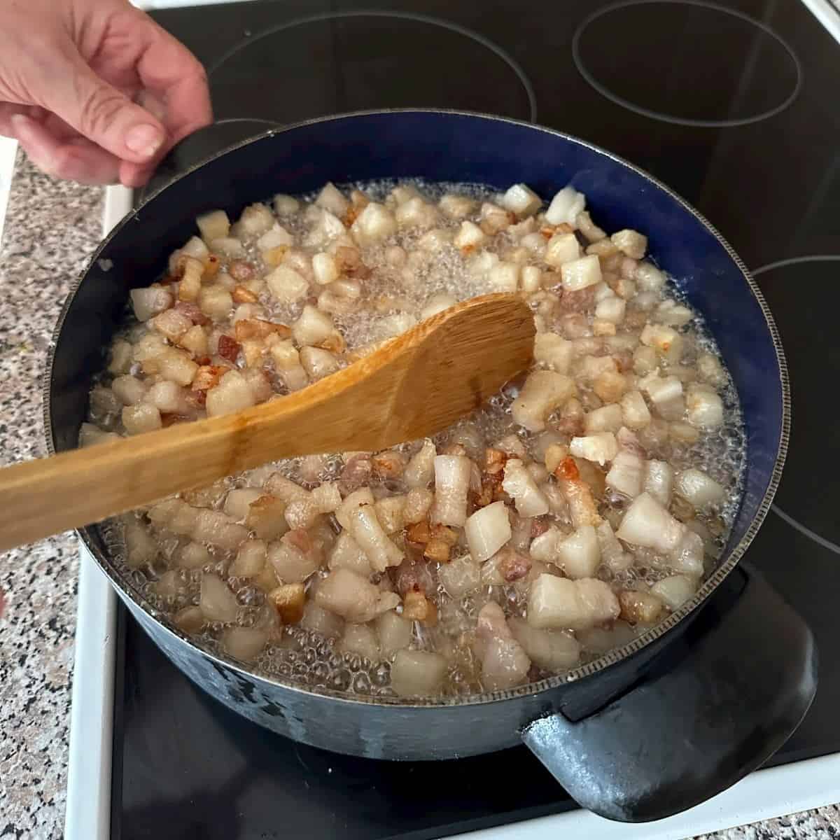 Mixing pork fat with a wooden spoon, rendering lard.