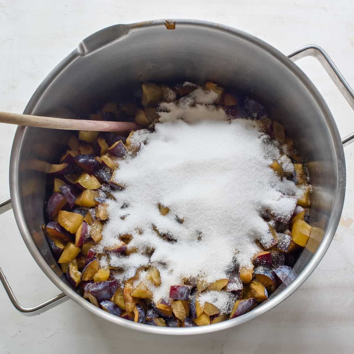 Pieces of plums sprinkled with lots of sugar, in a large pot.