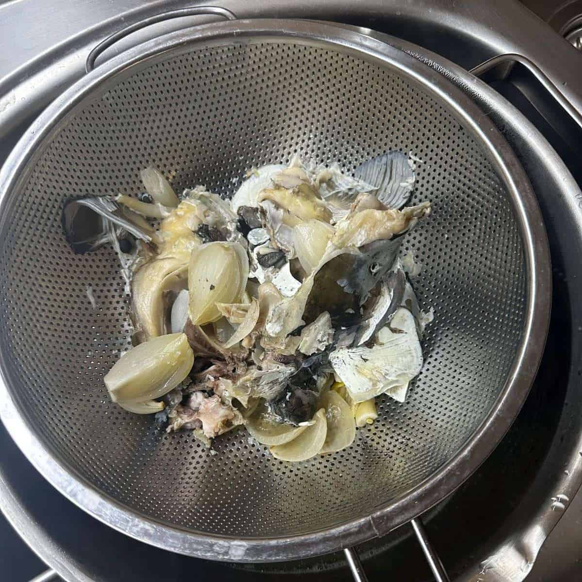 Fish head, onions, and seasonings drained in a stainless steel colander, ready for Czech cuisine.