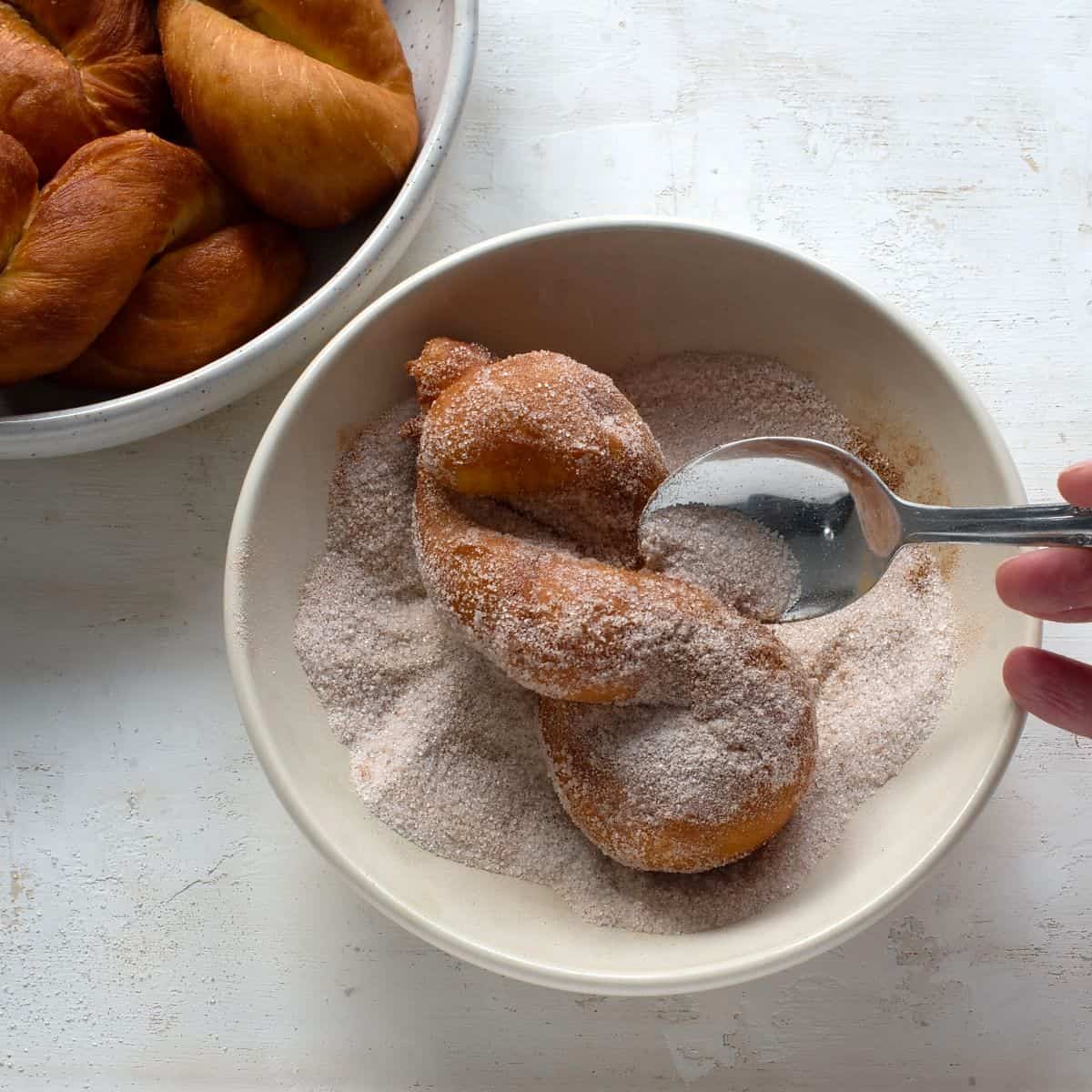 Coating fried šišky twists in cinnamon sugar.