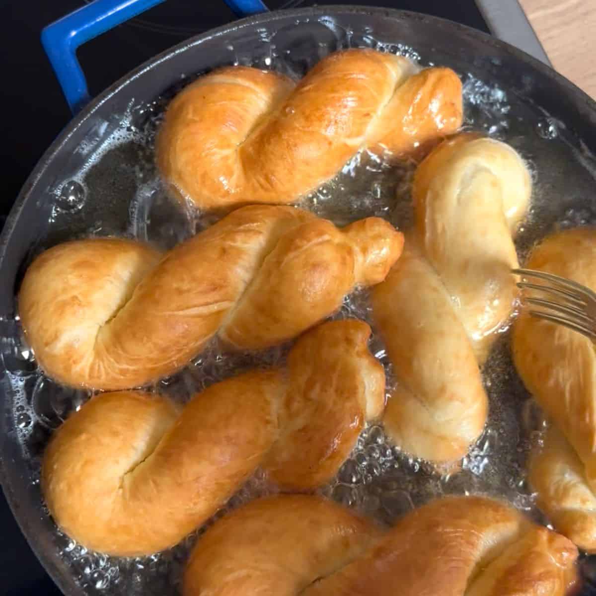 Frying šišky twists in a pan of oil.