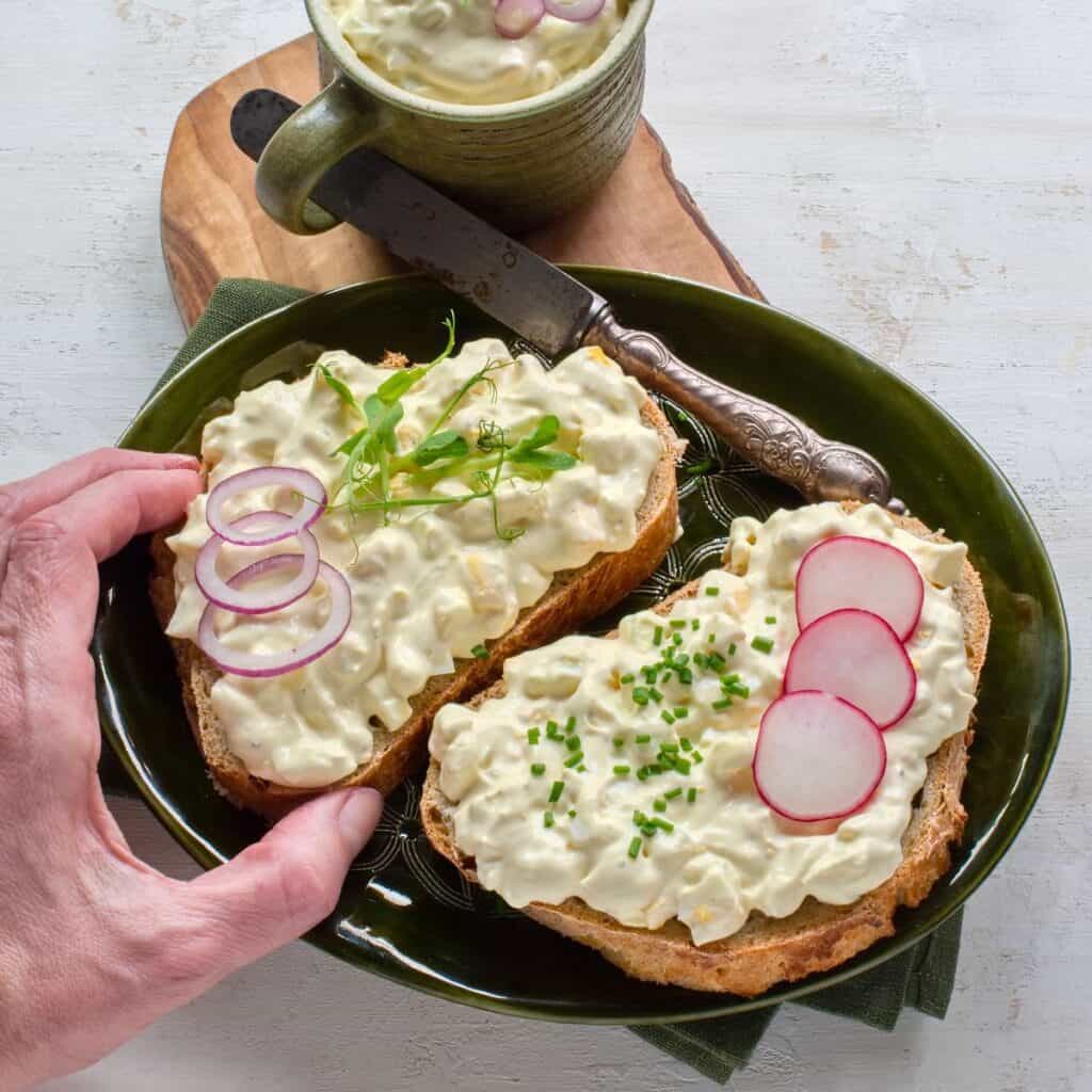 Czech egg salad (vajíčkový salát) topped on two slices of bread, garnished with red onion, radishes and greens.