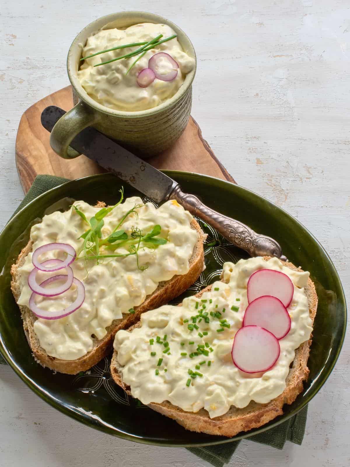 Czech egg salad (vajíčkový salát) topped on two slices of bread, garnished with red onion, radishes and greens.