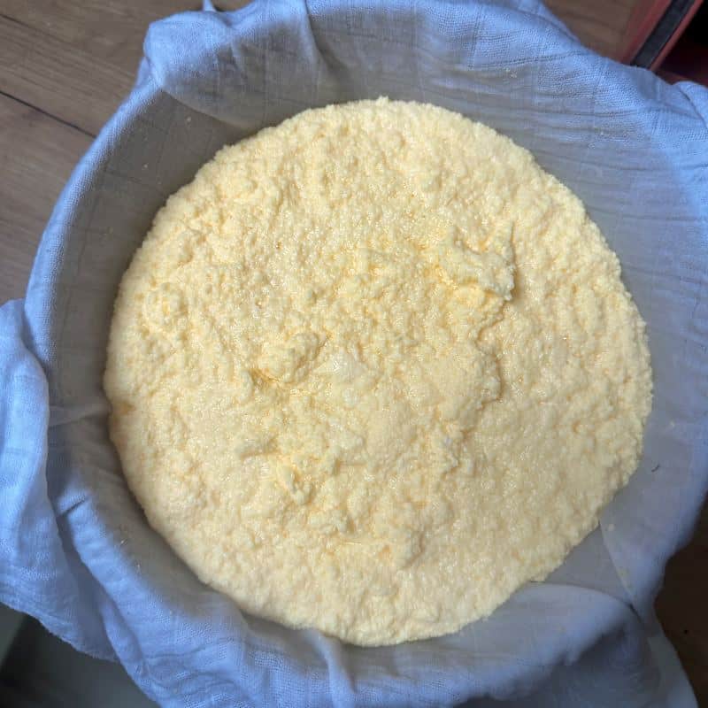 Curdled hrutka cheese in a sieve lined with a cloth.