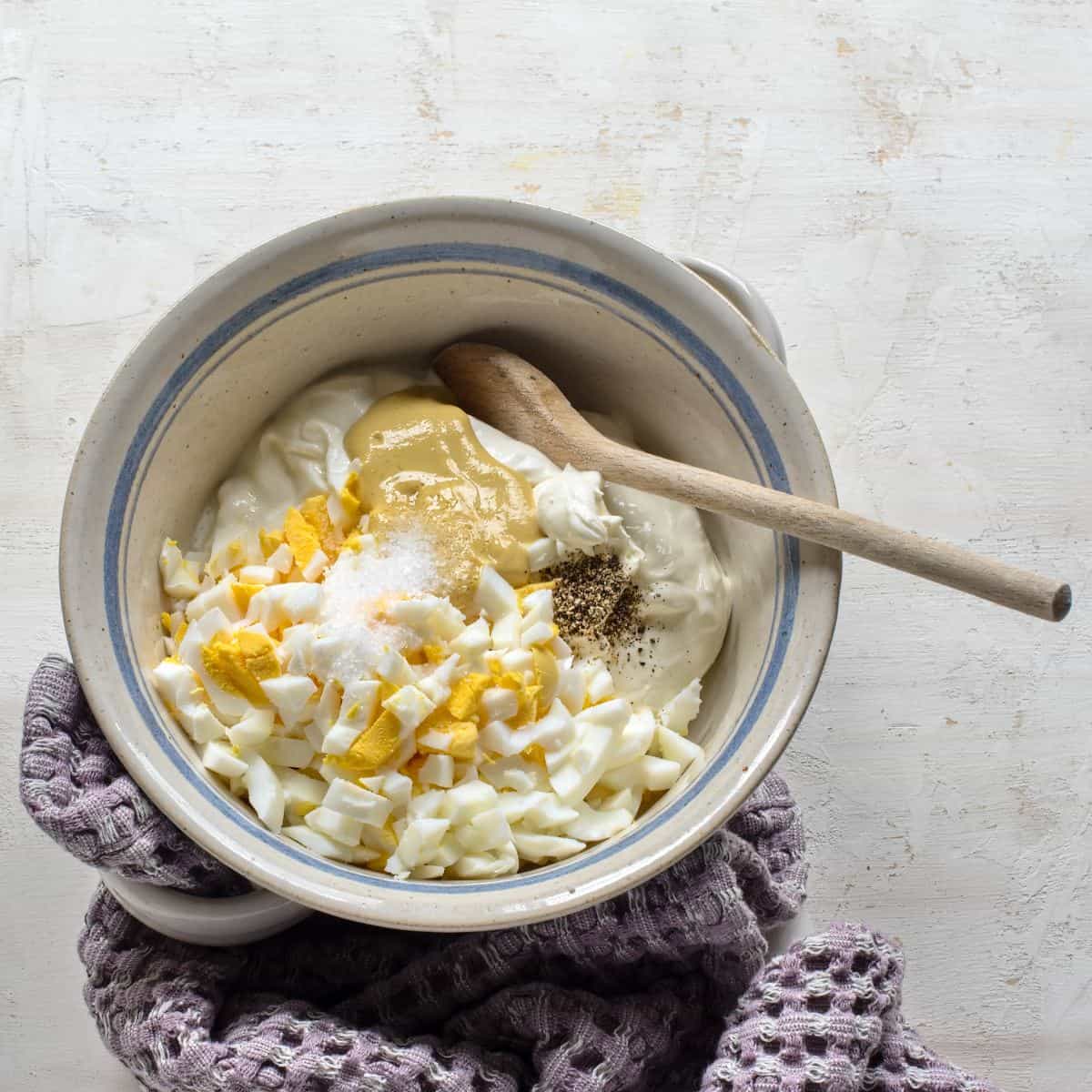 Making Czech egg salad - vajíčkový salát. Ingredients in a bowl with a wooden spoon.