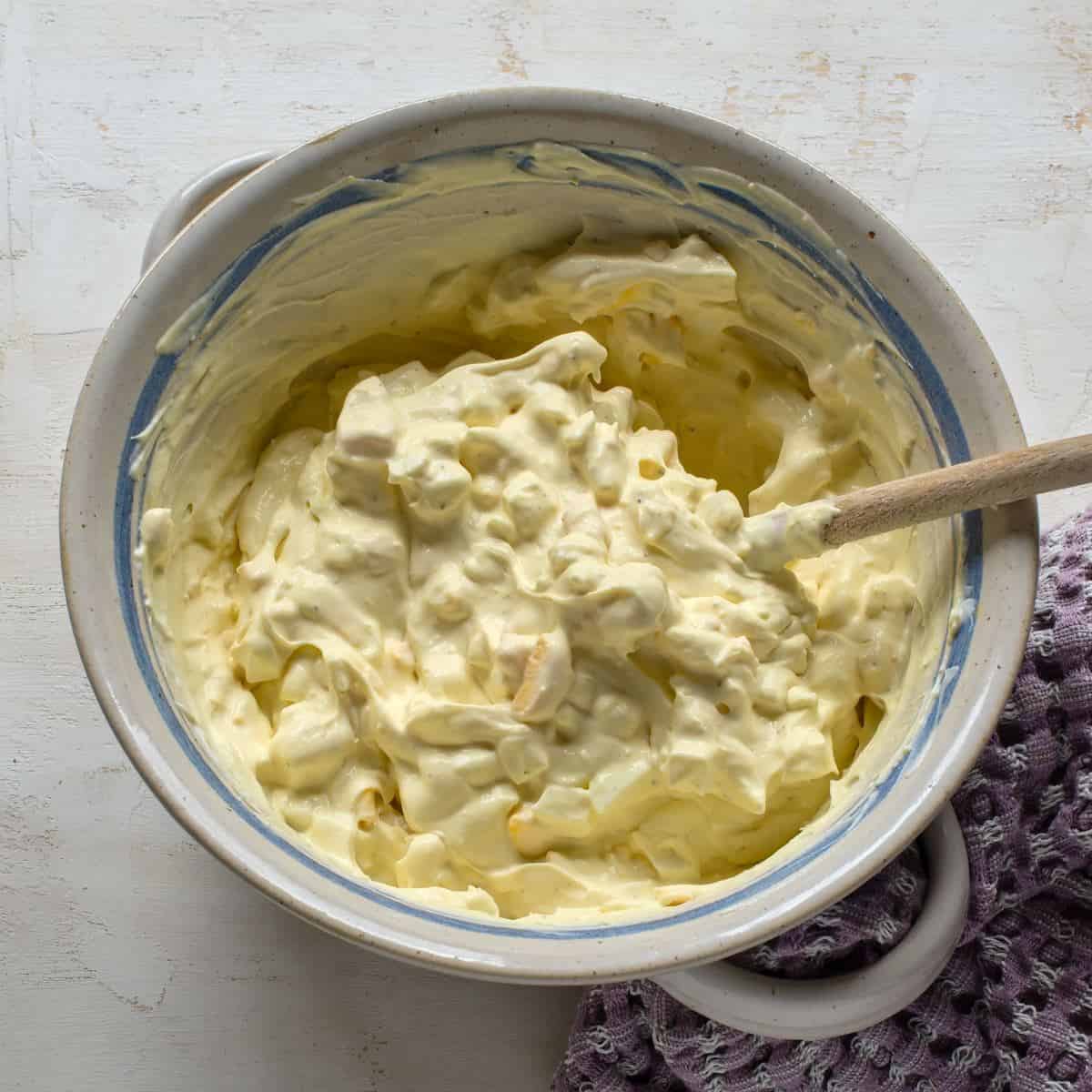 Making Czech egg salad - vajíčkový salát. Ingredients stirred in a bowl with a wooden spoon.