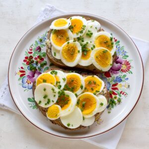 Two Czech bread slices smeared with butter, topped with sliced hard-boiled eggs. Served on a colorful plate.