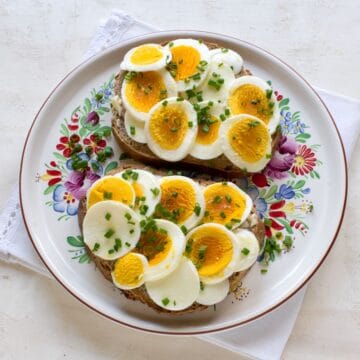 Two Czech bread slices smeared with butter, topped with sliced hard-boiled eggs. Served on a colorful plate.