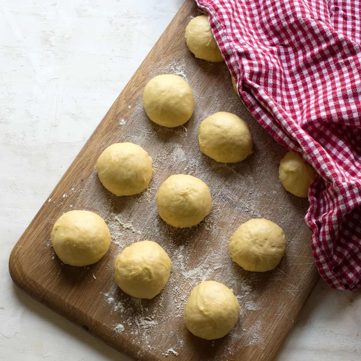 Dough ball for Czech jidáše, on a wooden board, resting under a red kitchen towel.