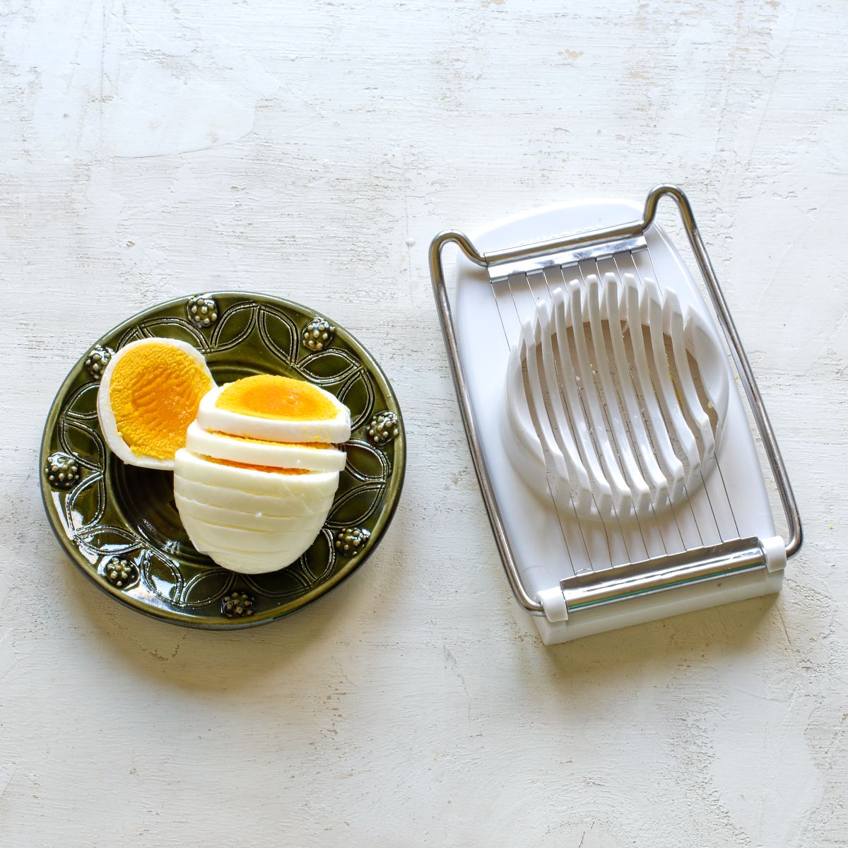 Egg slicer with sliced egg on a small green plate.