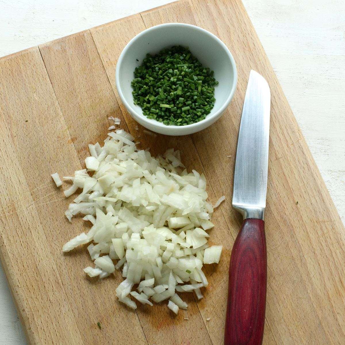 Chopped chives and onions on a wooden board.