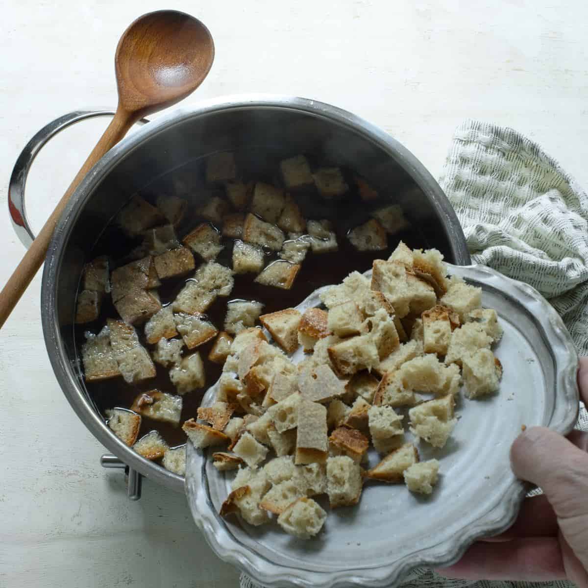 Adding cubed bread to a bowl of soup.