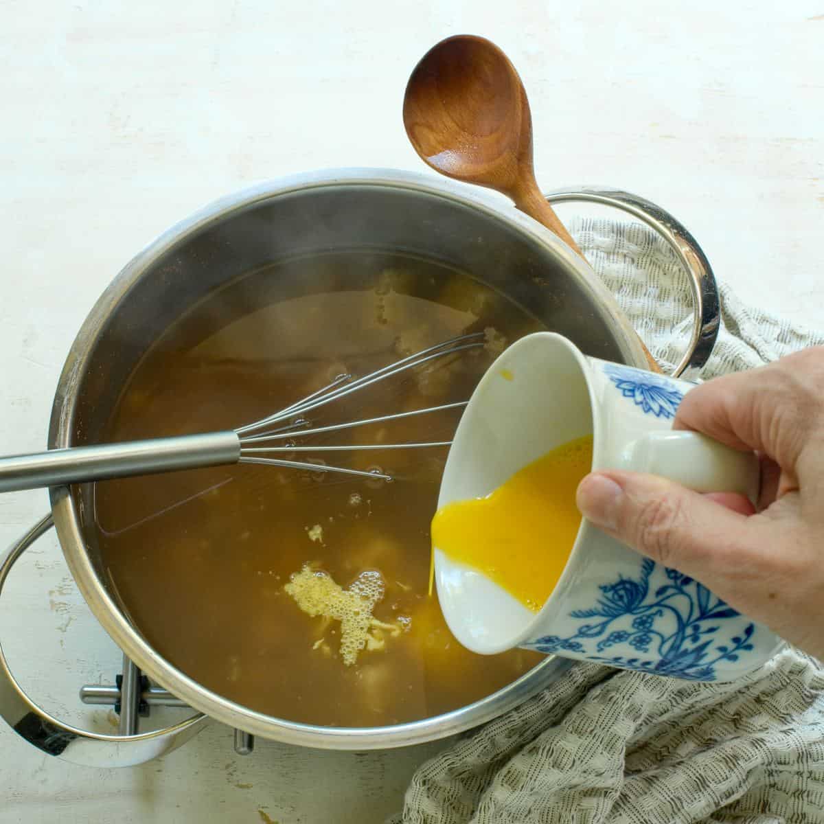 Adding whisked eggs to the pot of bread soup.