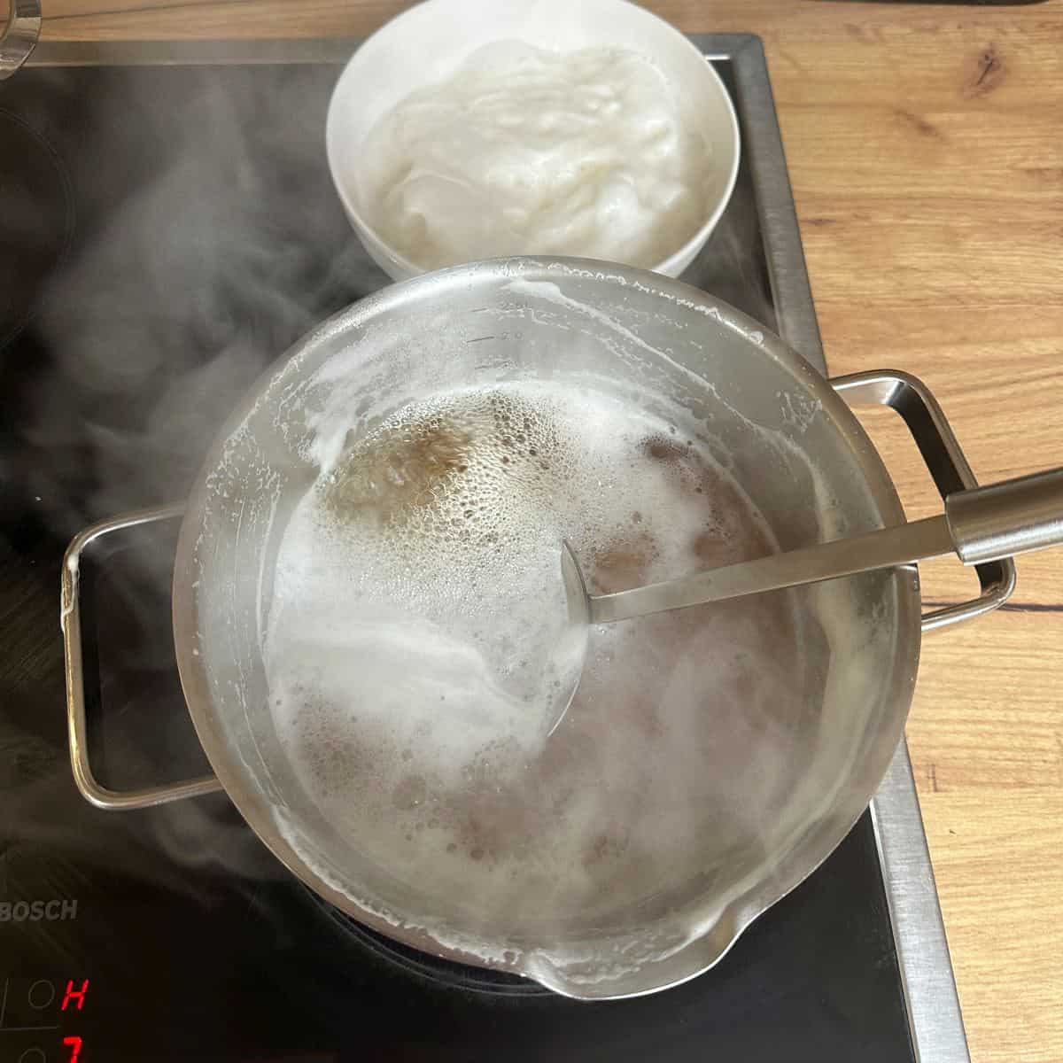 Skimming off foam from the surface of beer boiling in a saucepan.