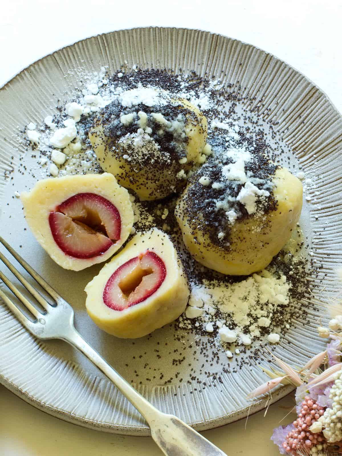 Czech potato dumplings with plums, topped with sweetened poppy seeds and drizzled with melted butter. Served on a plate.