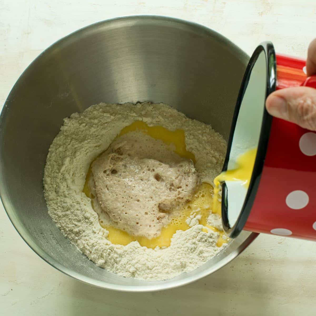 Pouring melted butter mixture to a bowl with flour and activated yeast.